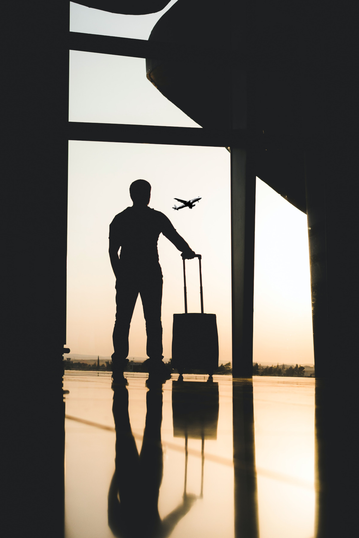 a person with luggage stands at an airport window, watching a plane take off